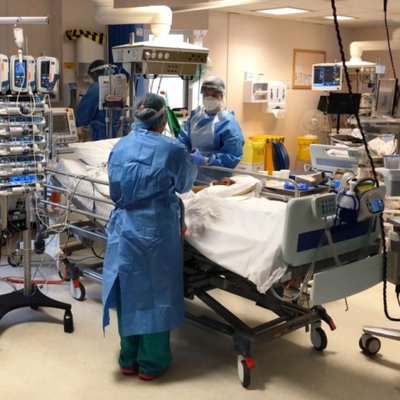 Shot of two staff members in full PPE in the critical care unit standing around a bed with a patient caring from him