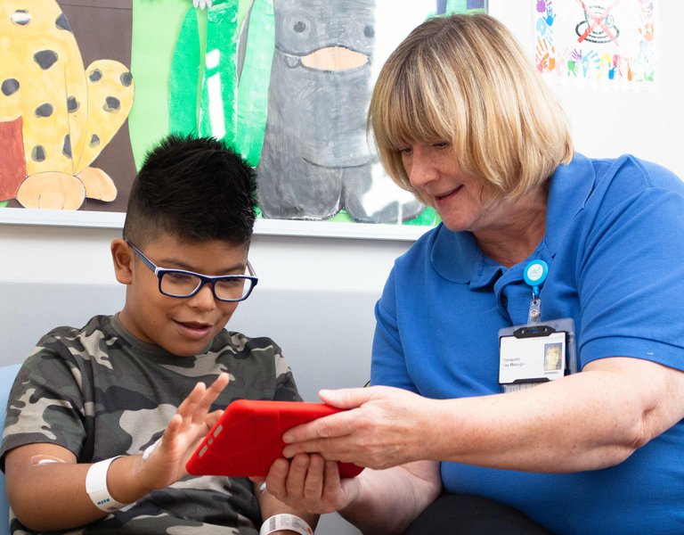 Boy playing on ipad accompanied by hospital staff
